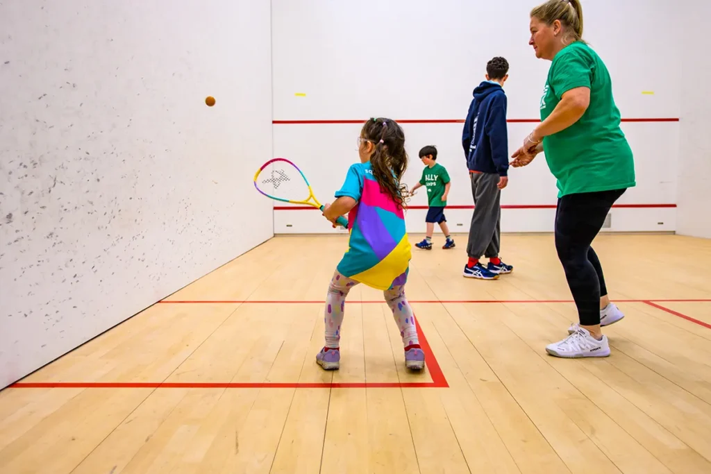 Young girl playing squash during a junior session with a coach providing guidance.