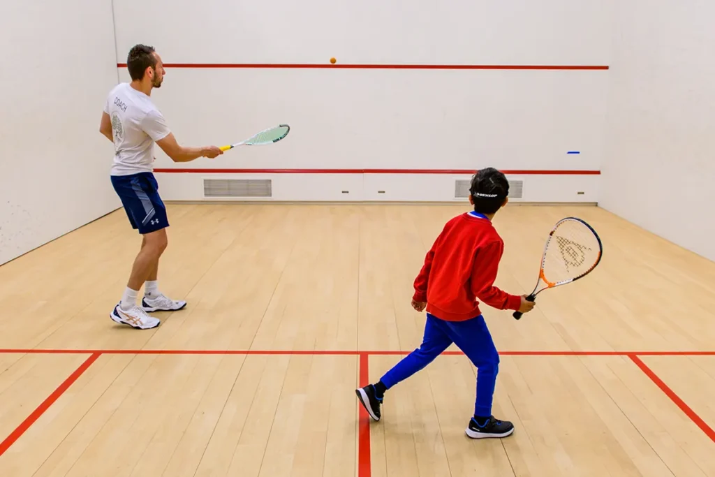 Squash coach and young player practising together on court, mid-rally.