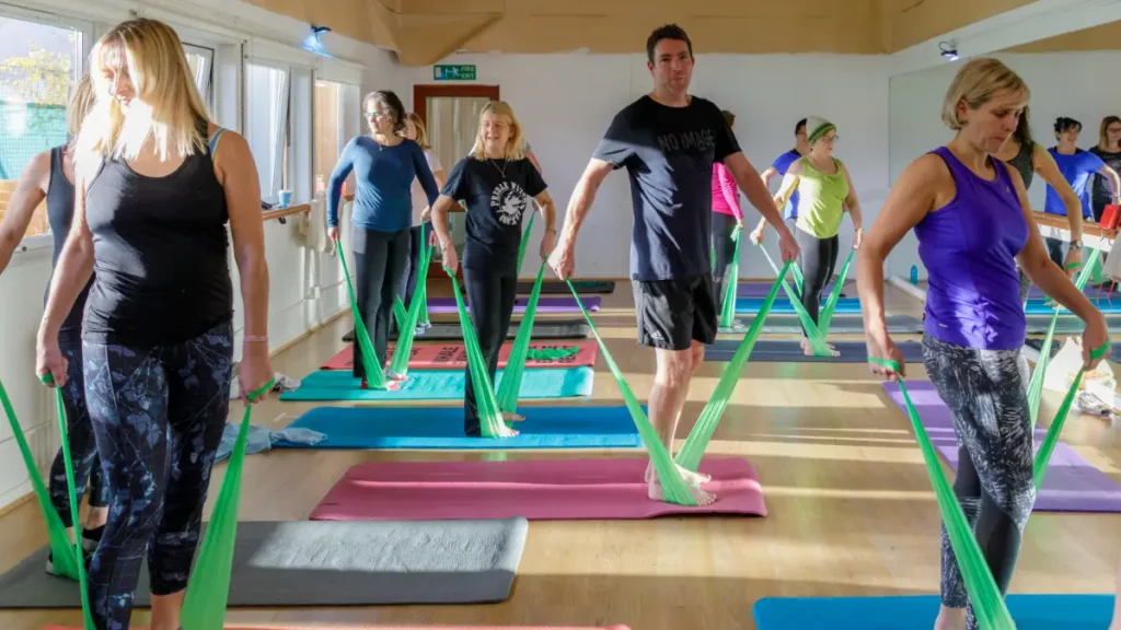 Group fitness class using resistance bands on yoga mats in a bright studio.