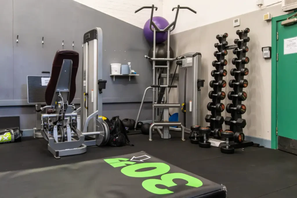 Compact gym corner with strength machines, a dumbbell rack, medicine balls, and plyometric equipment.