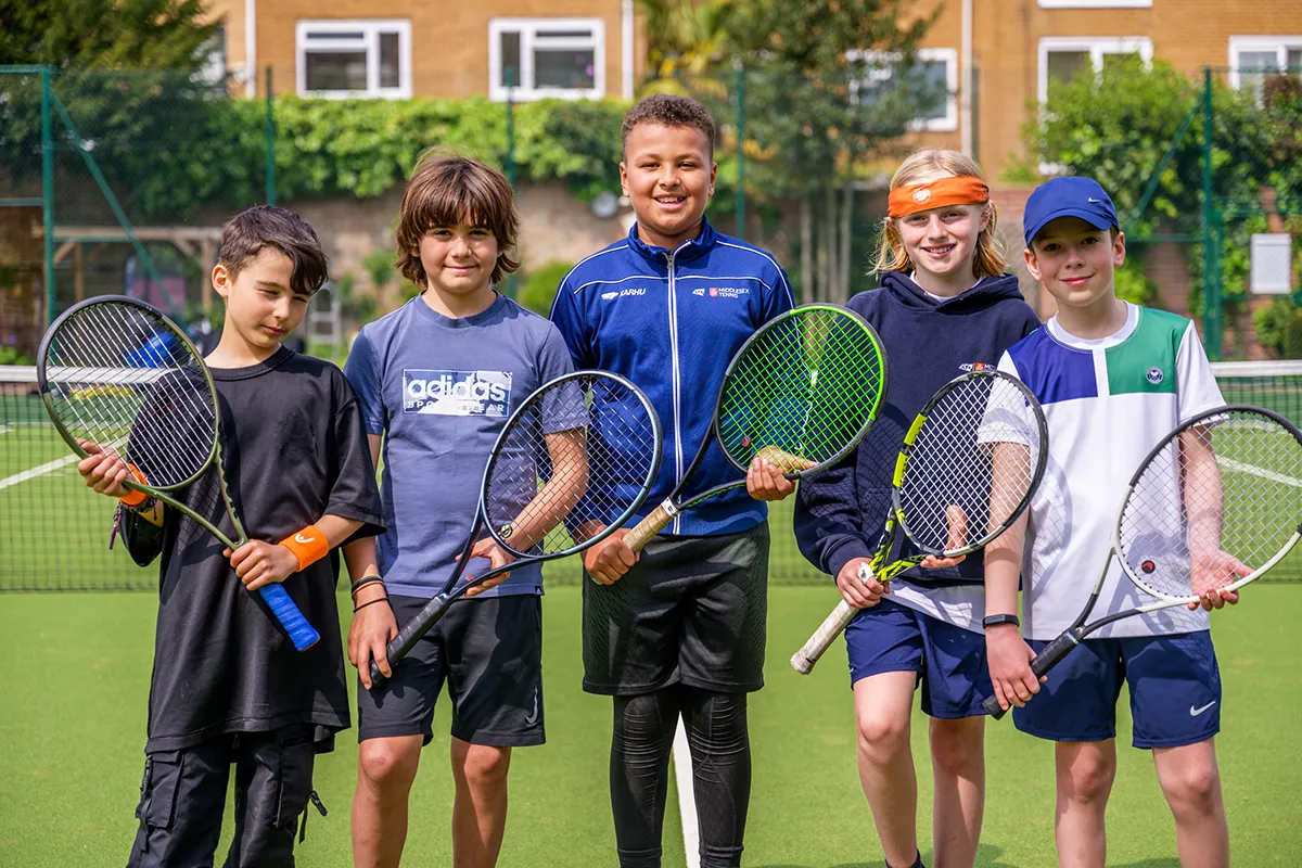 A group of children holding tennis rackets on court during a junior holiday tennis camp at Coolhurst Tennis Club.