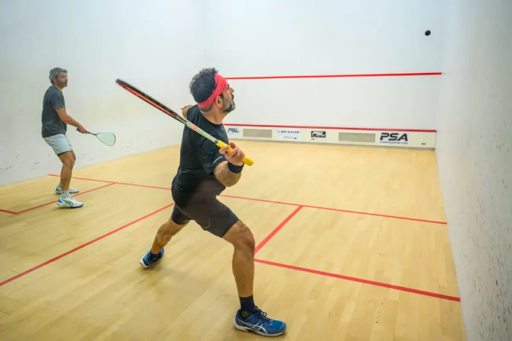Two men playing a squash match on an indoor court, one preparing to strike the ball.