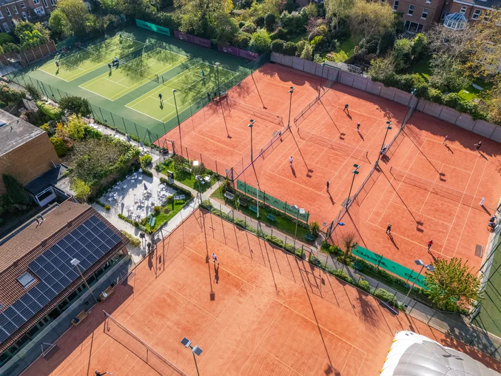 Aerial view of Coolhurst sports club showing multiple outdoor tennis courts with players and a smaller fenced padel court on a sunny day.